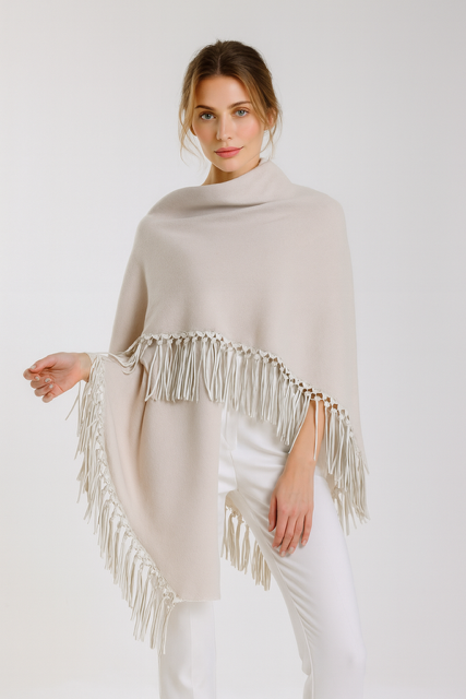 Woman wearing a beige poncho with fringe details on a white background
