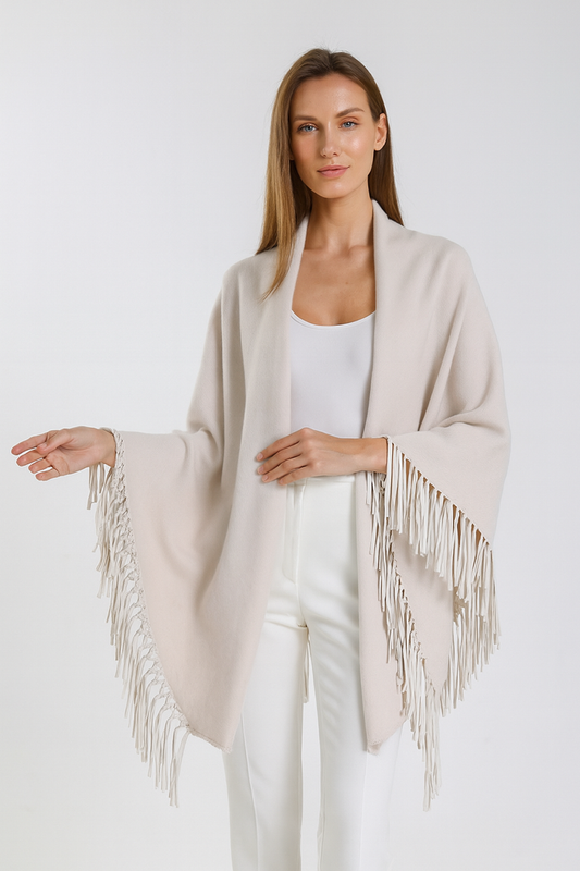 Woman wearing a beige fringe poncho over a white outfit on a plain background