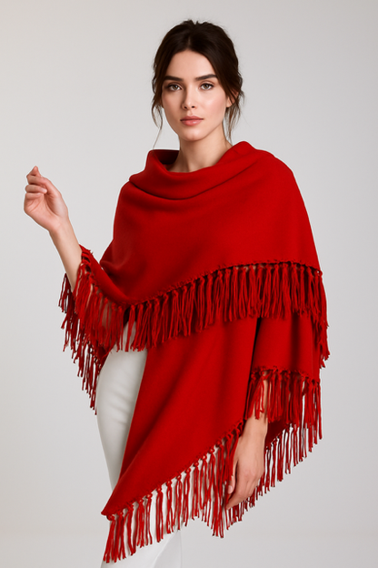 Woman wearing a red poncho with fringe details on a plain background